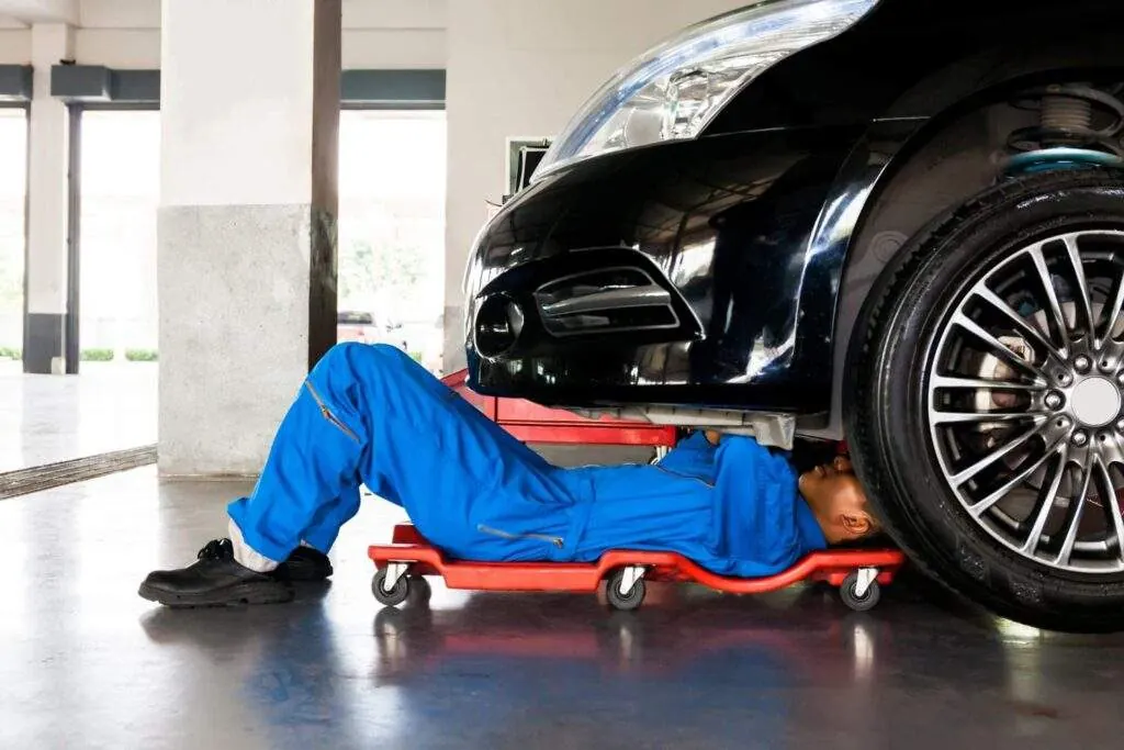 Mecánico con mono azul trabajando tumbado bajo un coche en un taller